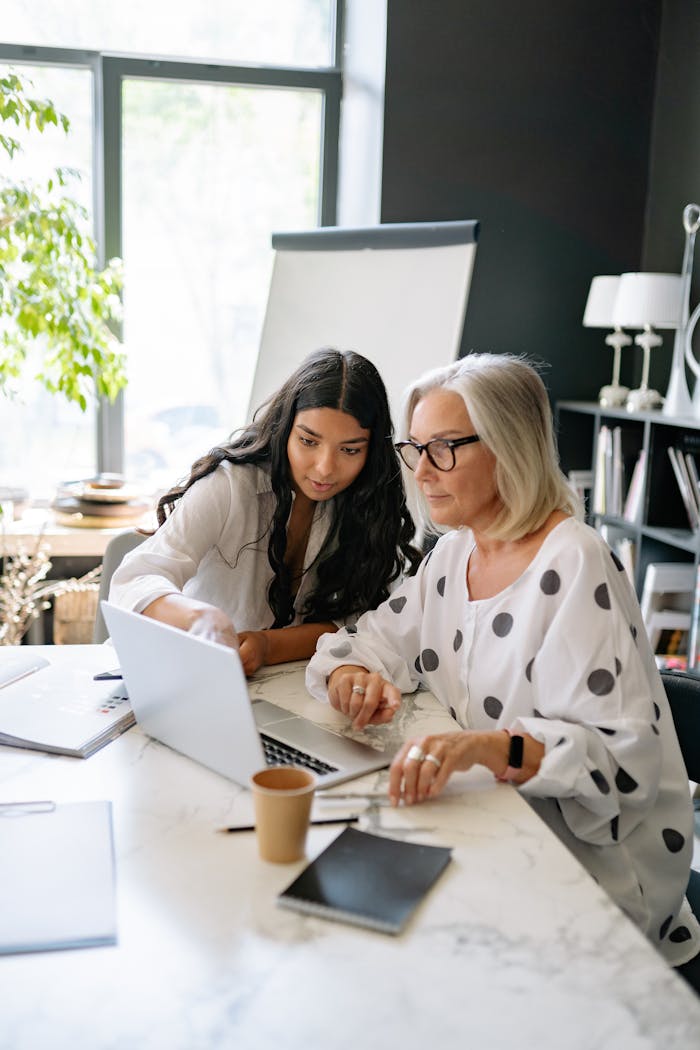 Two professional women collaborating on a project with a laptop in a modern office setting.